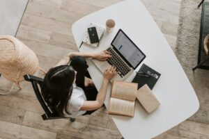 Vue aérienne d'une femme utilisant un ordinateur portable à un bureau à la maison, entourée de livres, d'un téléphone et d'une tasse.