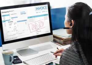 Professionnelle avec casque vérifiant une facture marquée "PAYÉE" sur un système de facturation en ligne